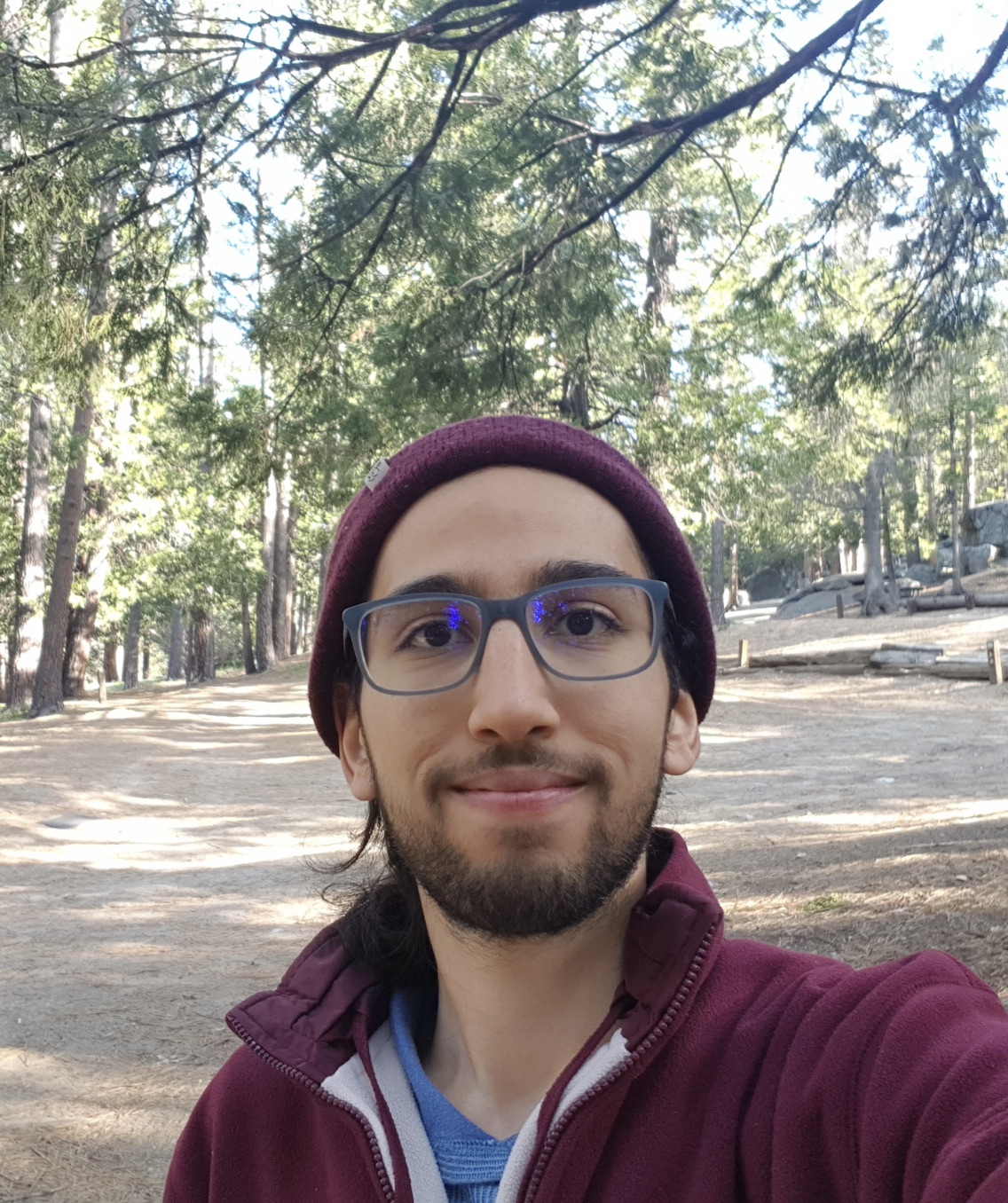 portrait of Farouk Ghodhbane smiling in a wilderness trail surrounded by tall pine trees